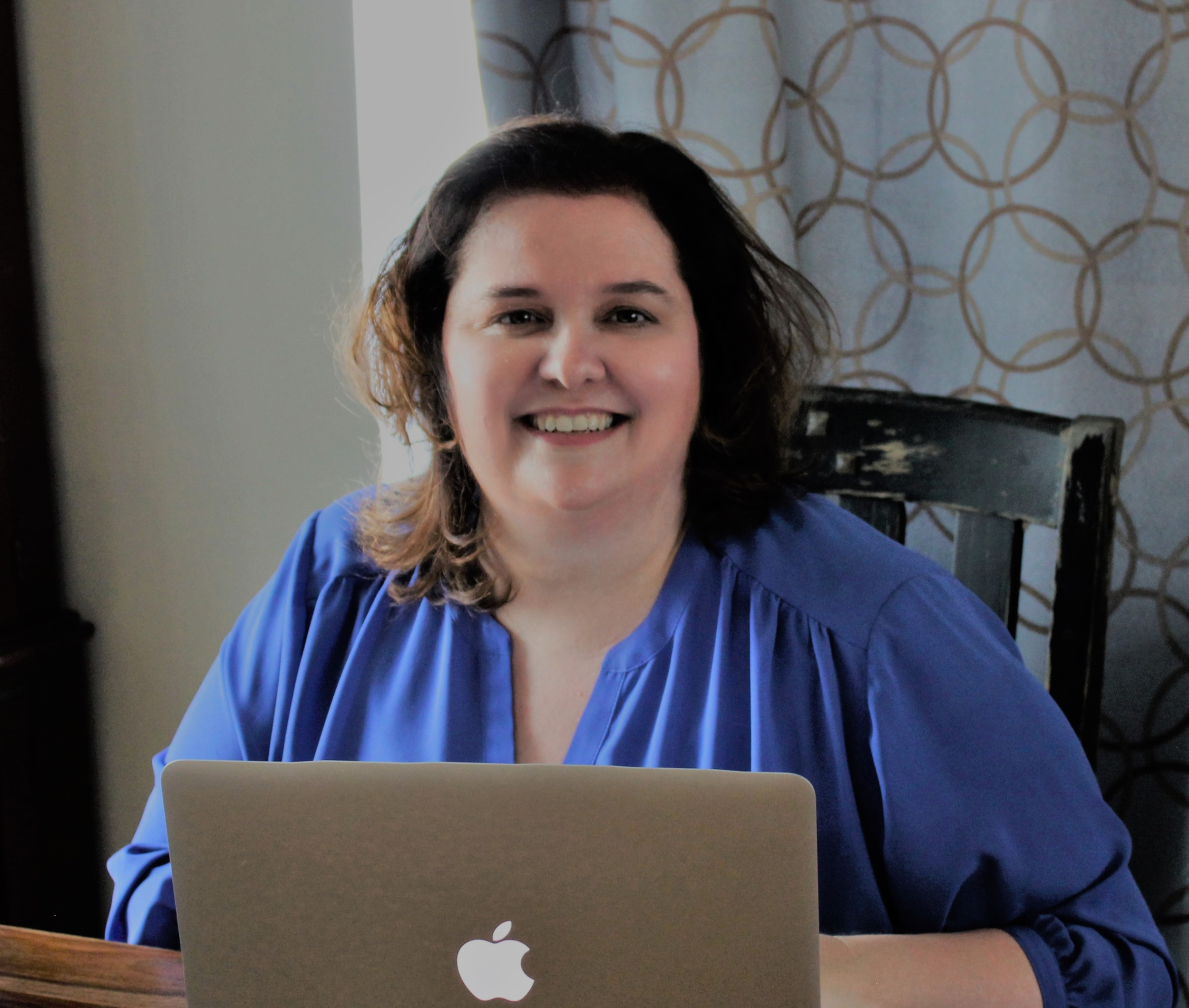  Photo of Darby Kane in a bright blue shirt sitting behind an apple laptop. Photo by Charissa McAfee 