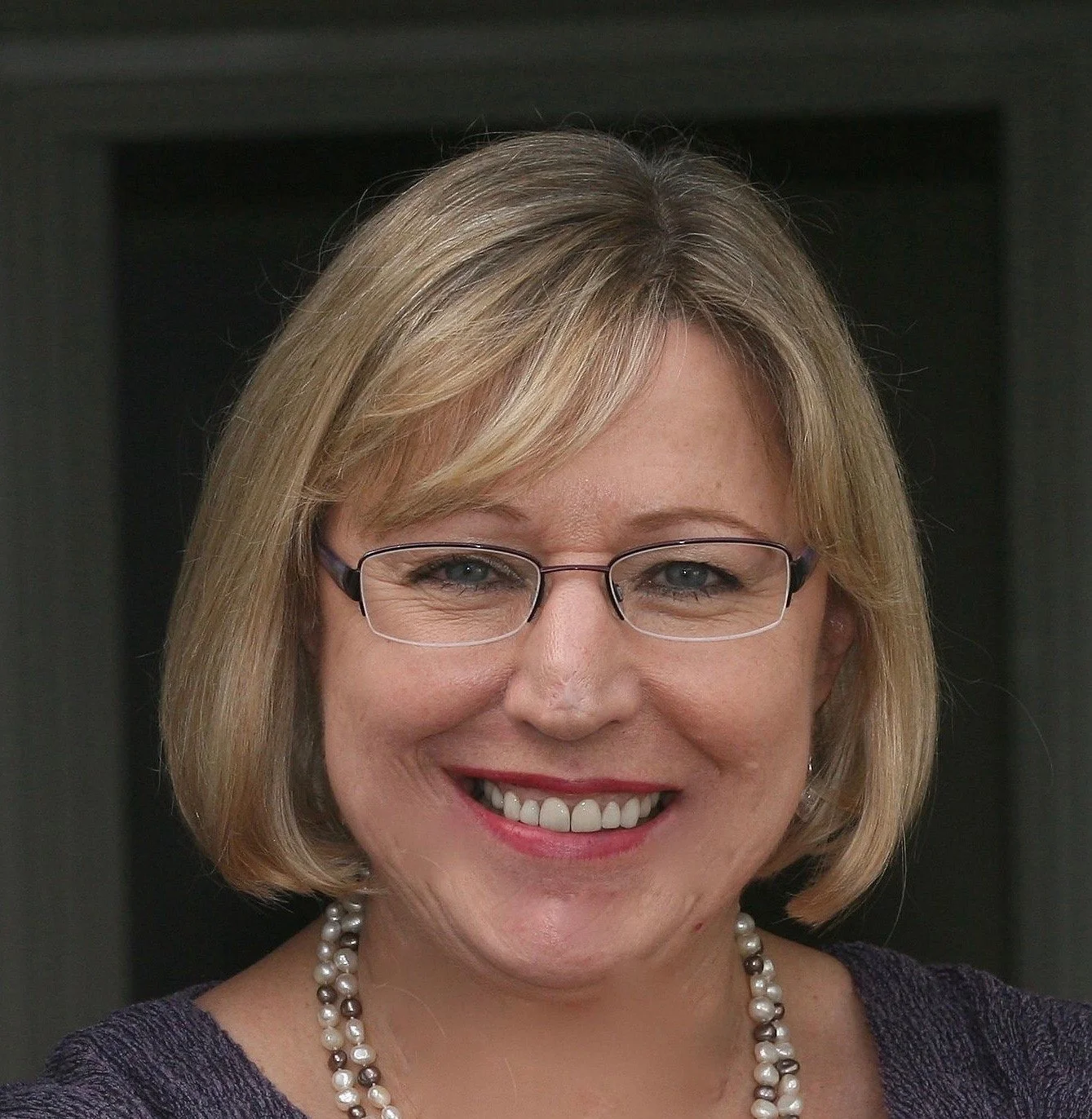 Flora Harding headshot, Flora has blonde shoulder length hair, she is smiling, and wearing glasses